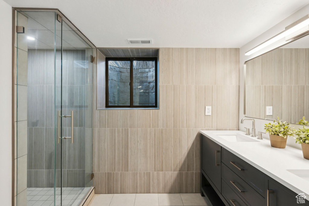 Full bathroom with a sink, double vanity, tile walls, visible vents, and a shower stall