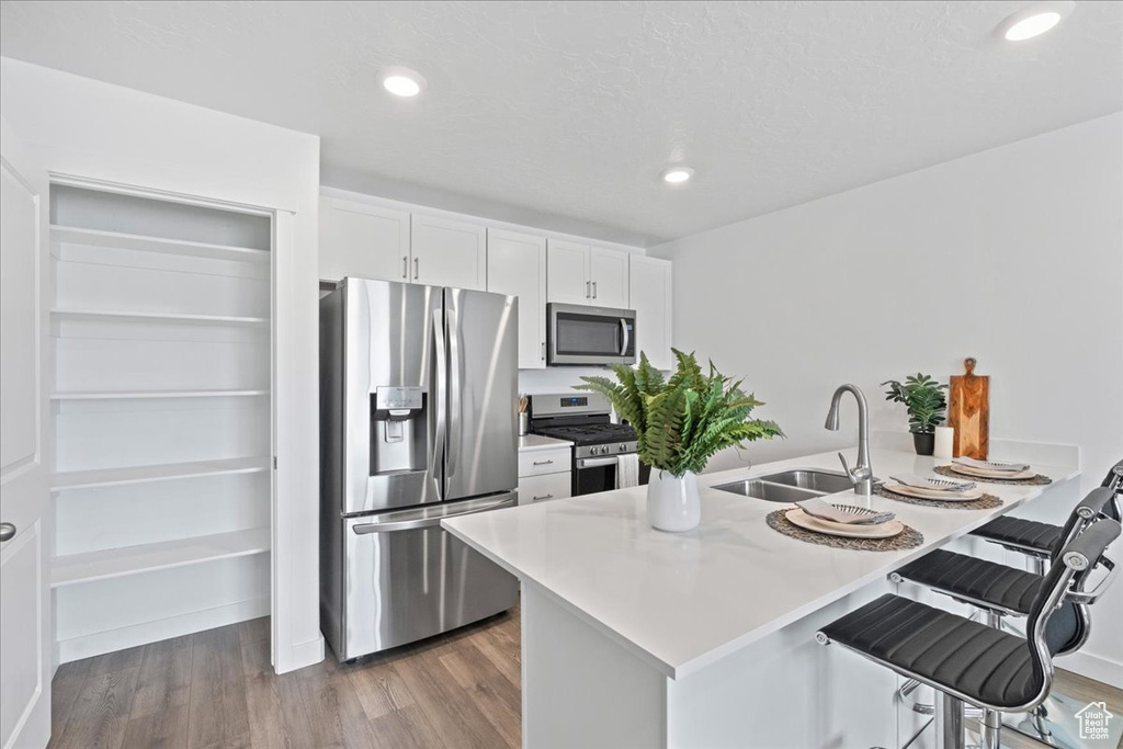 Kitchen featuring appliances with stainless steel finishes, a breakfast bar, a peninsula, dark wood-style floors, and white cabinets