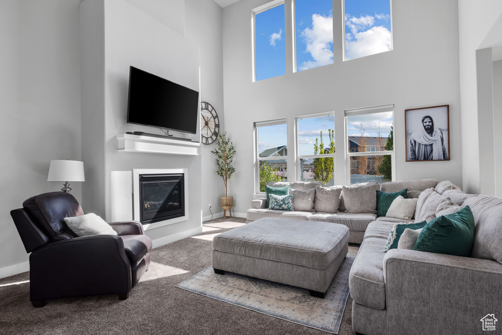 Living area with a high ceiling, a glass covered fireplace, carpet floors, and baseboards