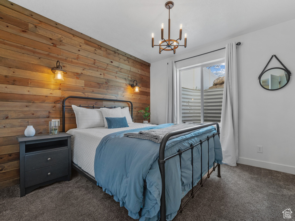Bedroom featuring baseboards, dark colored carpet, a chandelier, and wooden walls