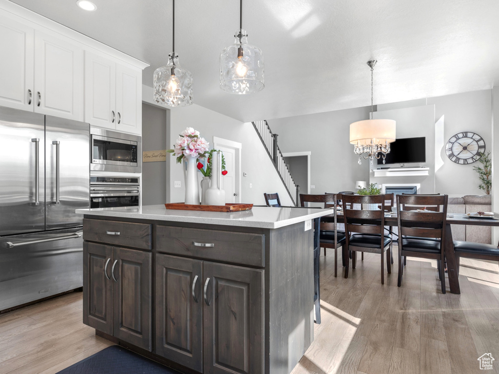 Kitchen with light wood finished floors, white cabinets, a chandelier, light countertops, and appliances with stainless steel finishes