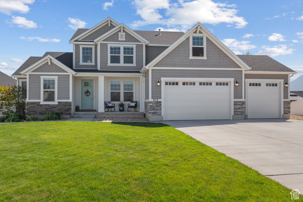 Craftsman-style house featuring stone siding, a porch, a front yard, and concrete driveway