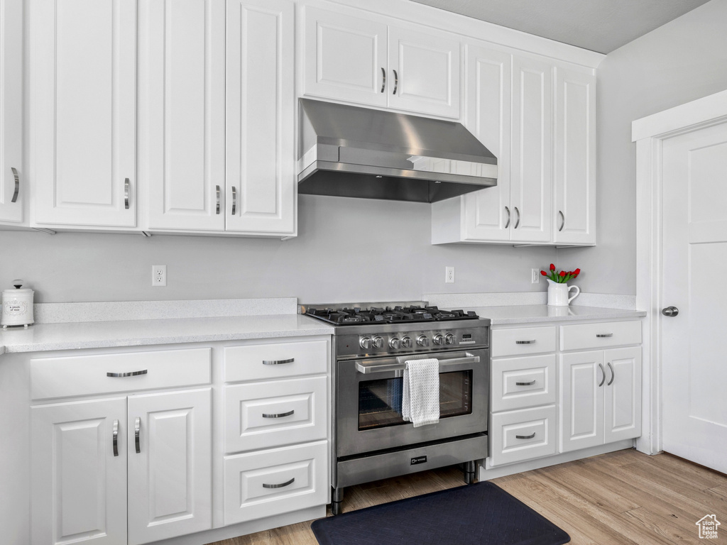 Kitchen with white cabinets, high end range, under cabinet range hood, and light countertops
