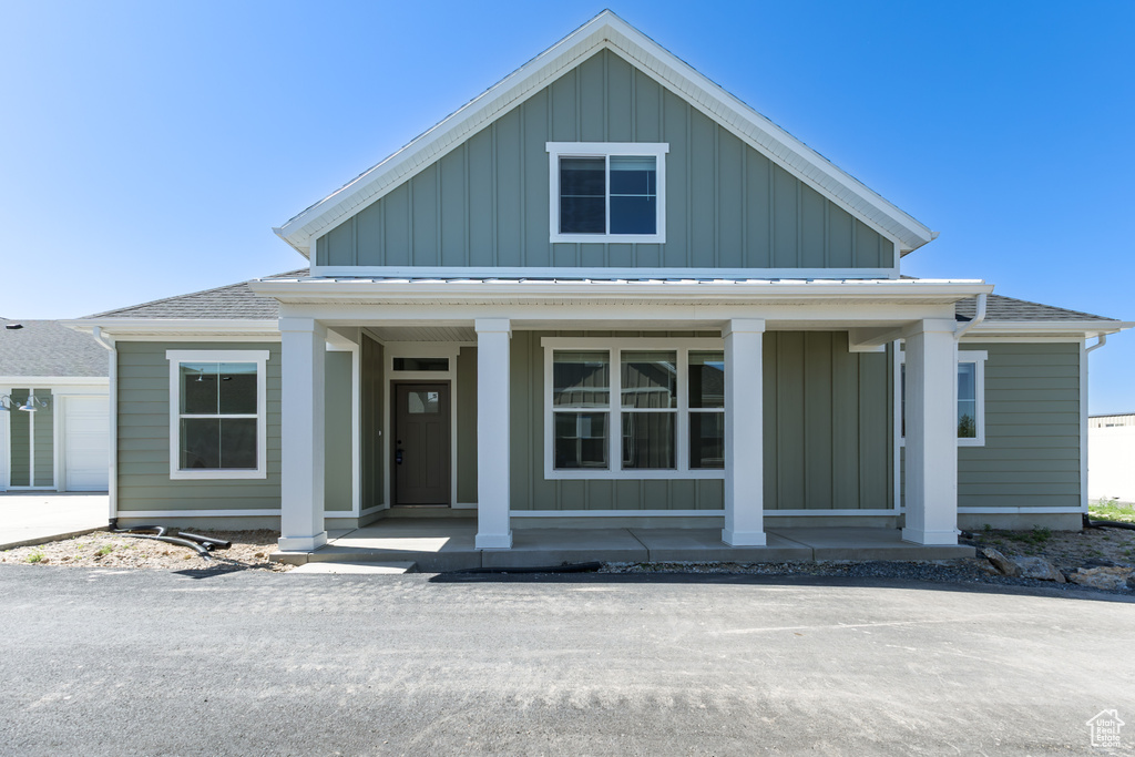 View of front of home with covered porch, board and batten siding, and roof with shingles