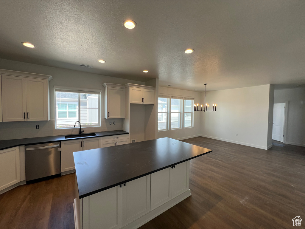 Kitchen with dark countertops, stainless steel dishwasher, a sink, a chandelier, and a wealth of natural light