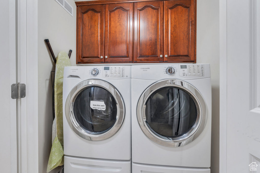 Laundry area featuring separate washer and dryer, visible vents, and cabinet space
