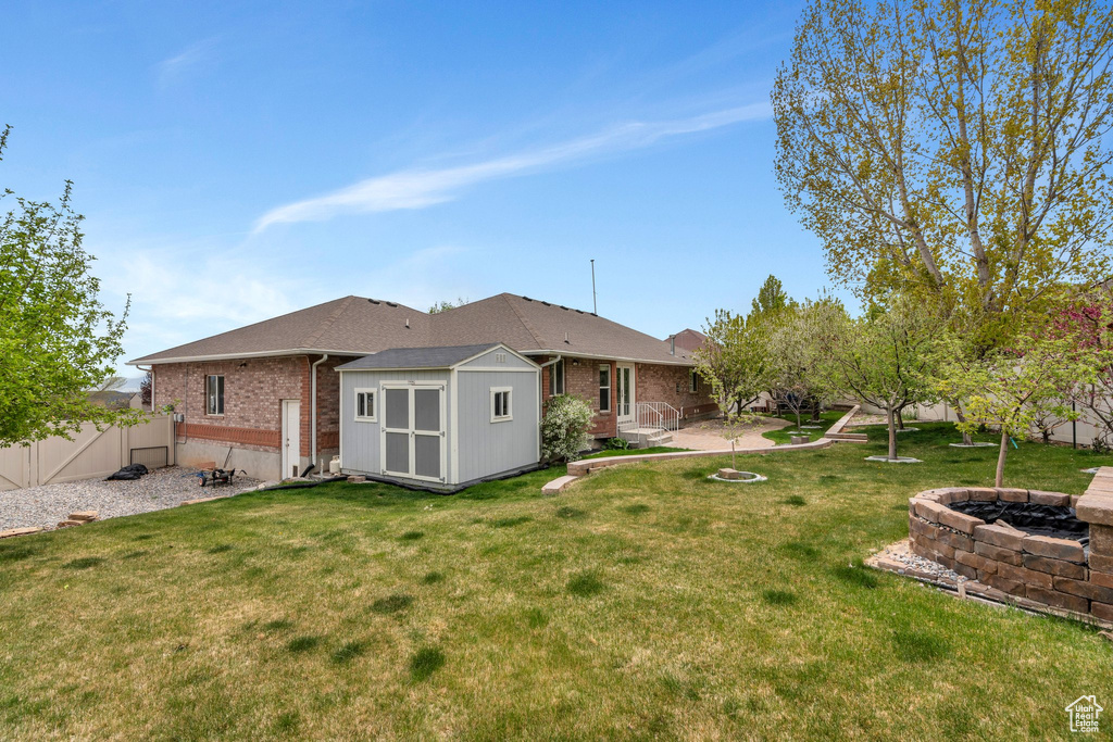 Rear view of house with a shed, a patio area, an outbuilding, an outdoor fire pit, and brick siding