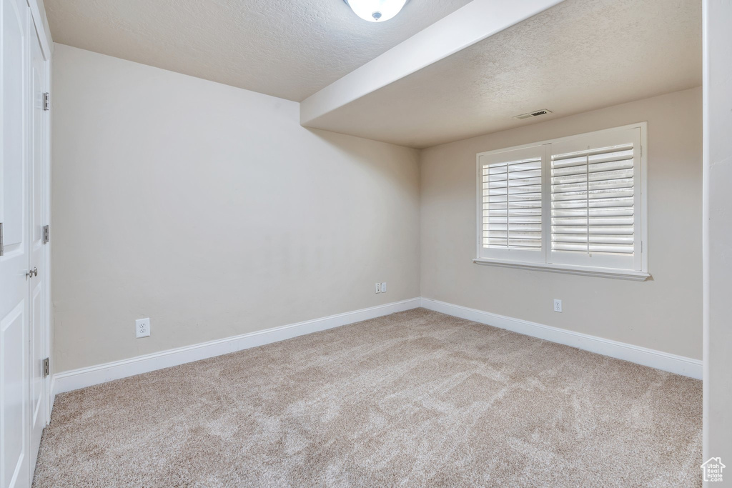 Carpeted spare room with baseboards, a textured ceiling, and visible vents