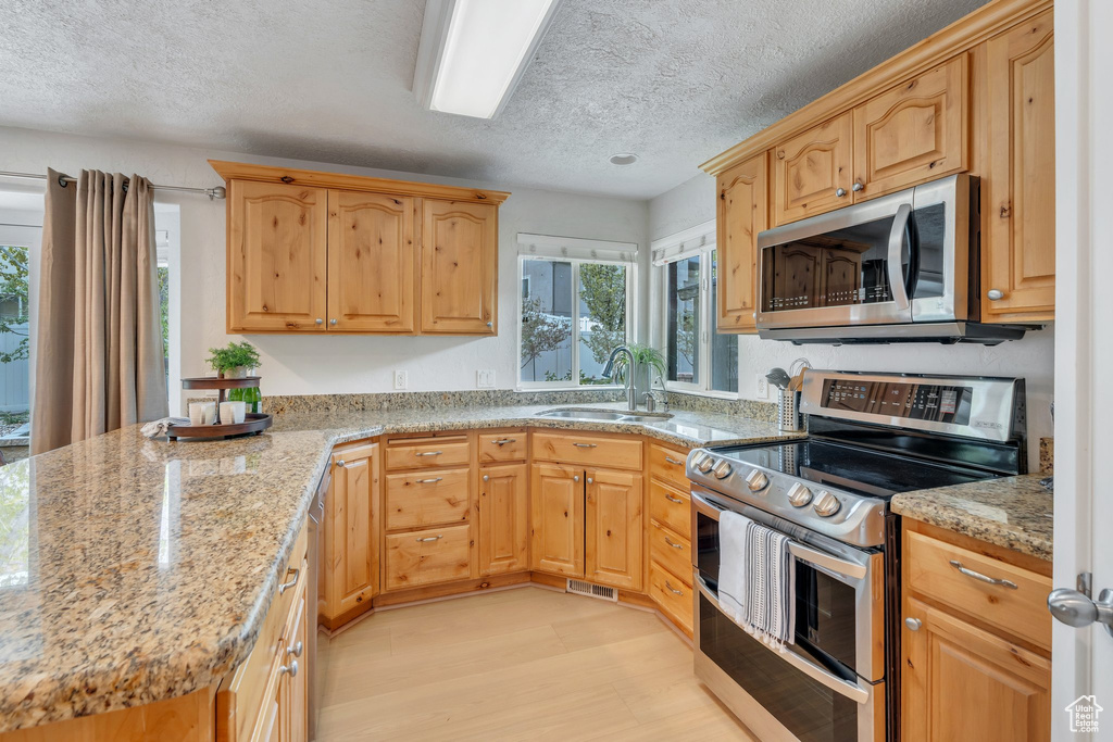 Kitchen with stainless steel appliances, a sink, light stone countertops, light wood-style flooring, and a textured ceiling