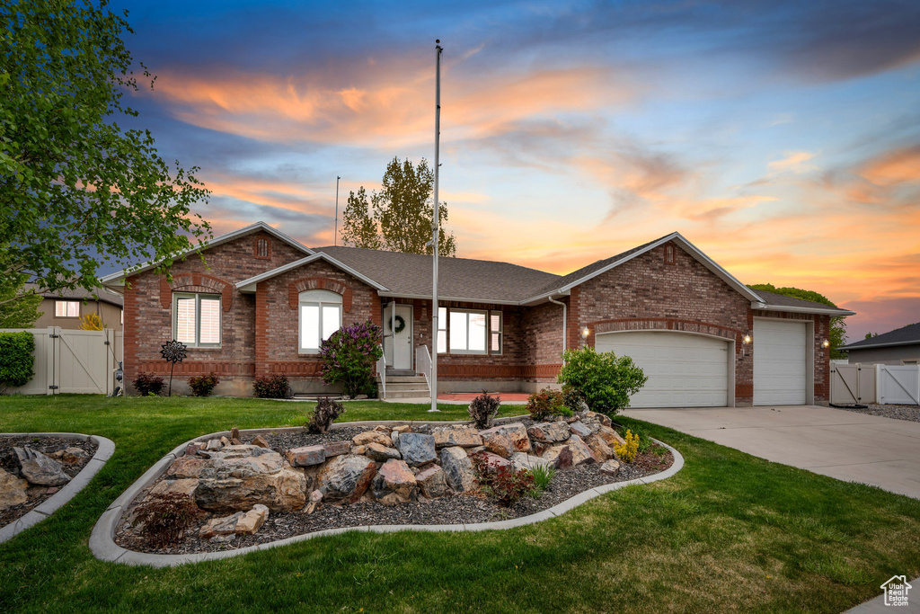 Single story home featuring a gate, concrete driveway, a lawn, a garage, and brick siding