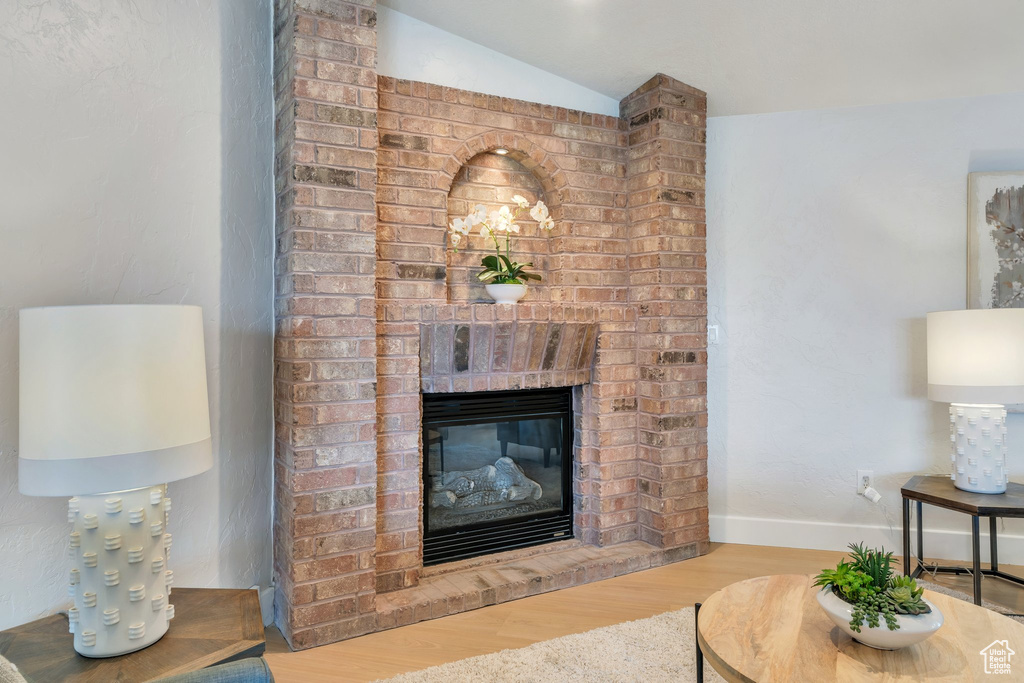 Living area with wood finished floors, a brick fireplace, lofted ceiling, and baseboards