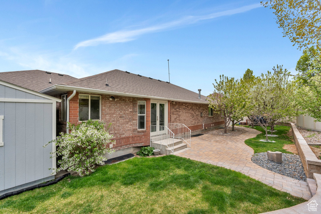 Back of property featuring a storage shed, french doors, an outbuilding, a lawn, and a shingled roof