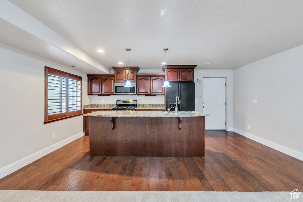 Kitchen with baseboards, an island with sink, stainless steel appliances, and dark wood-type flooring