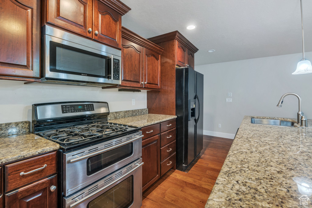Kitchen featuring dark wood finished floors, stainless steel appliances, a sink, pendant lighting, and baseboards