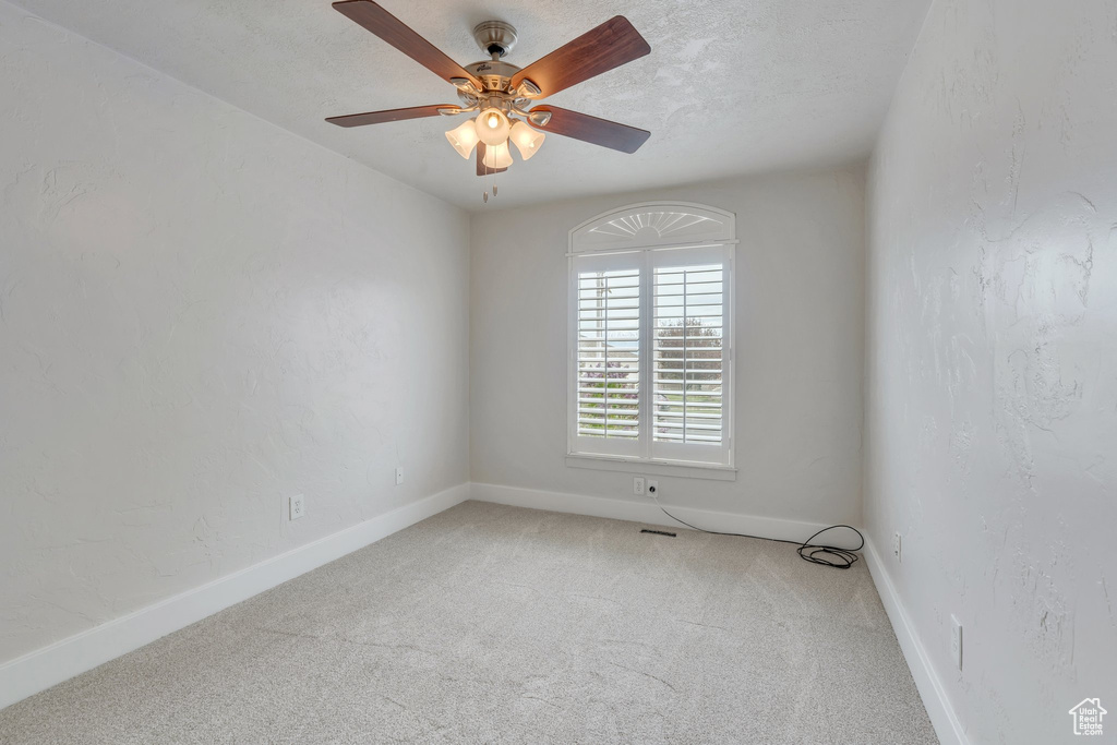 Carpeted spare room featuring ceiling fan and baseboards