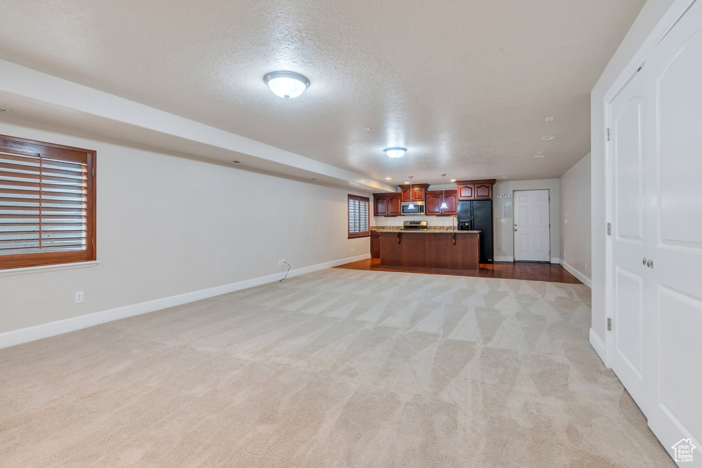 Unfurnished living room with light carpet, a textured ceiling, and baseboards