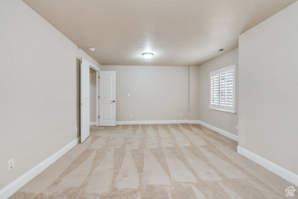Empty room with baseboards, a textured ceiling, light colored carpet, and visible vents