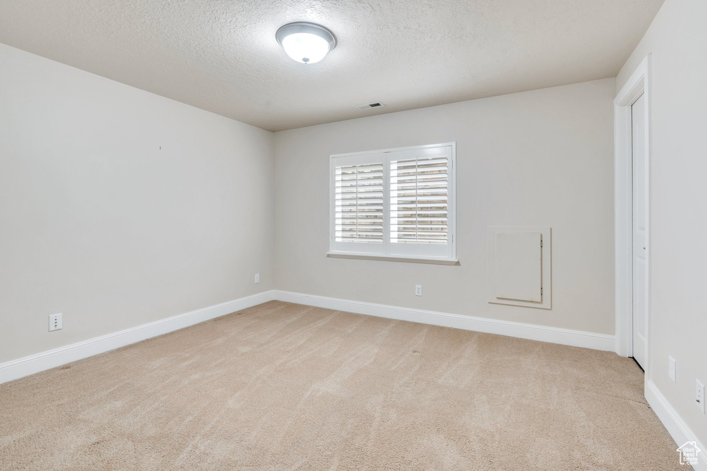 Carpeted spare room featuring baseboards, visible vents, and a textured ceiling