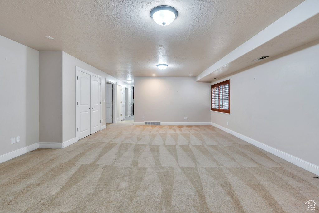 Basement with a textured ceiling, light carpet, and visible vents
