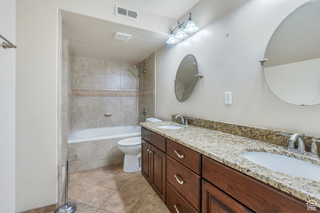 Bathroom with tiled shower / bath, visible vents, toilet, and a sink
