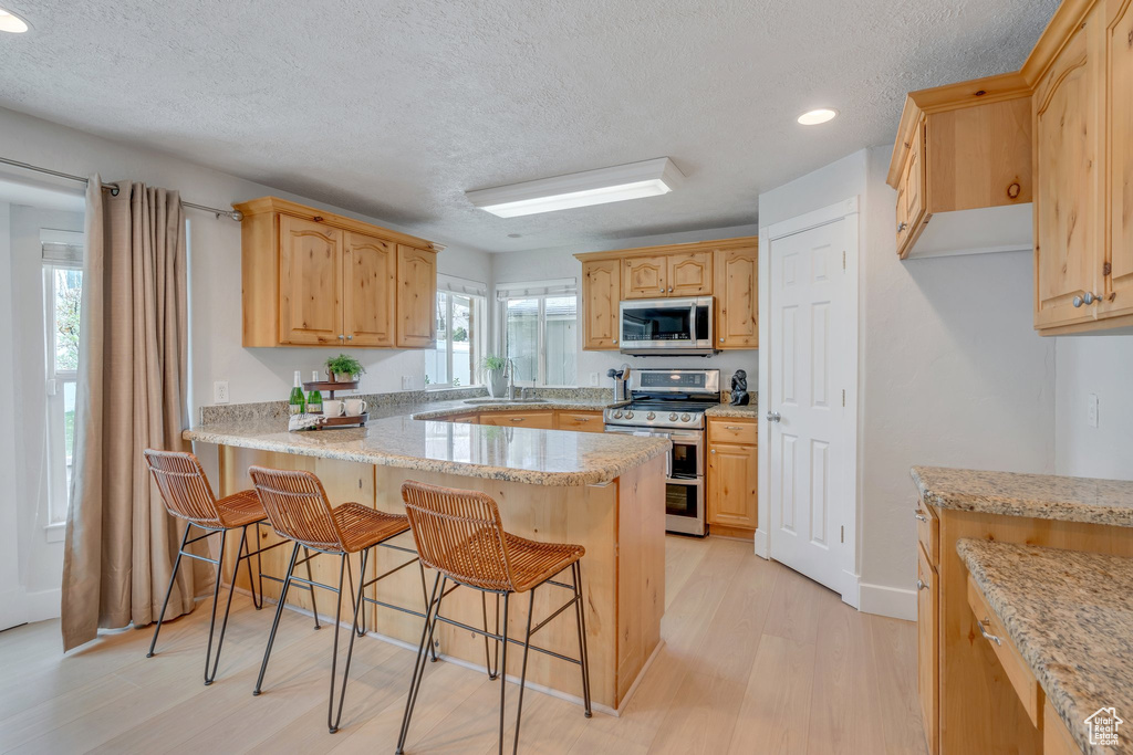 Kitchen with a peninsula, a kitchen breakfast bar, a textured ceiling, light wood-style floors, and appliances with stainless steel finishes