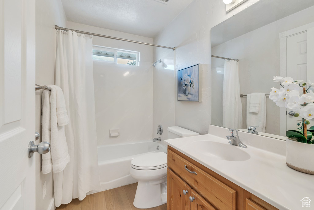 Full bathroom featuring toilet, vanity, wood finished floors, and shower / bathtub combination with curtain