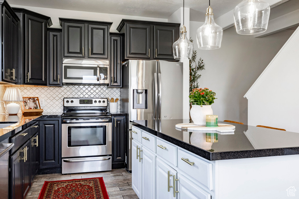 Kitchen featuring a center island, tasteful backsplash, stainless steel appliances, white cabinets, and dark cabinets