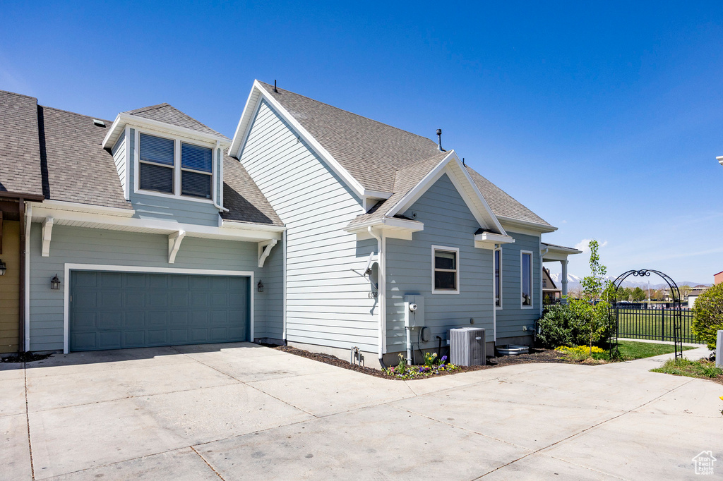 Back of house featuring fence, a shingled roof, cooling unit, driveway, and a garage
