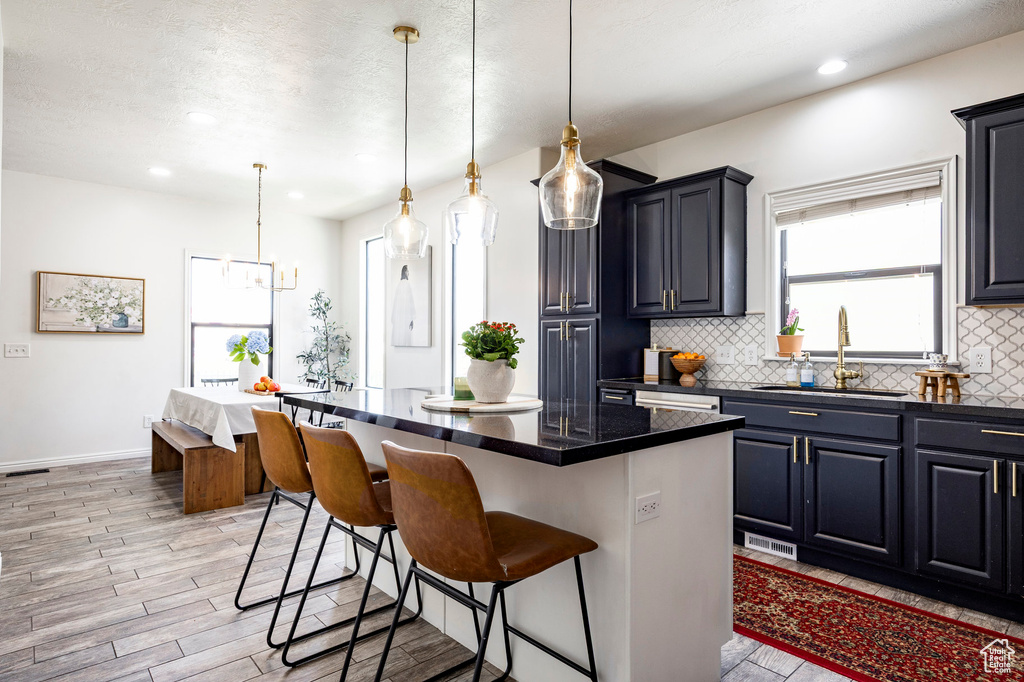 Kitchen featuring a kitchen breakfast bar, dark countertops, a sink, decorative backsplash, and light wood-style flooring