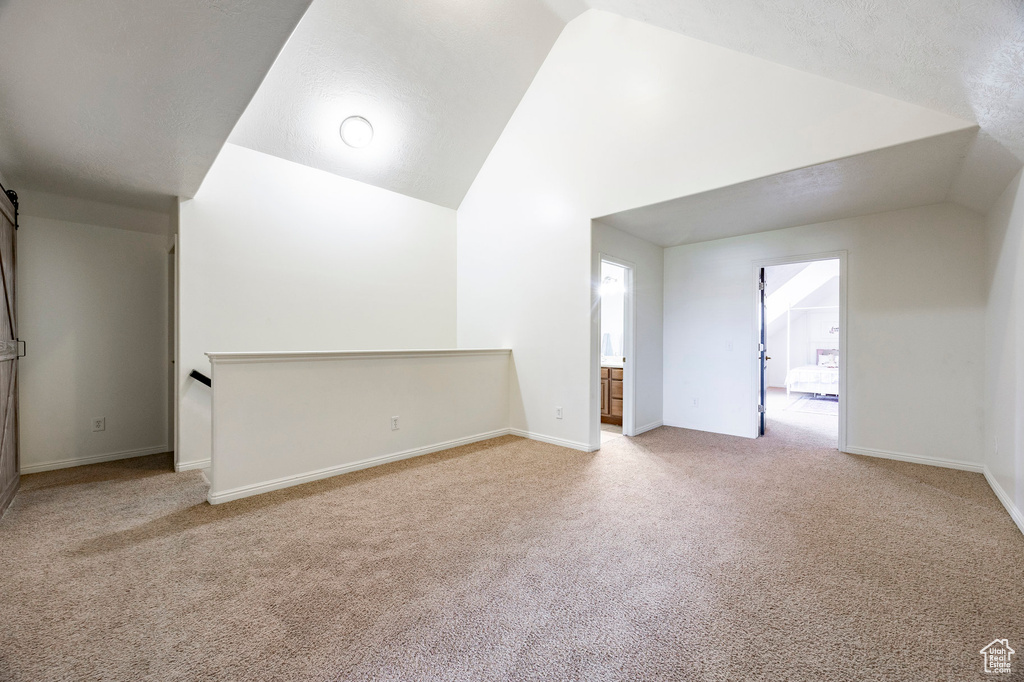 Additional living space with lofted ceiling, baseboards, and light carpet