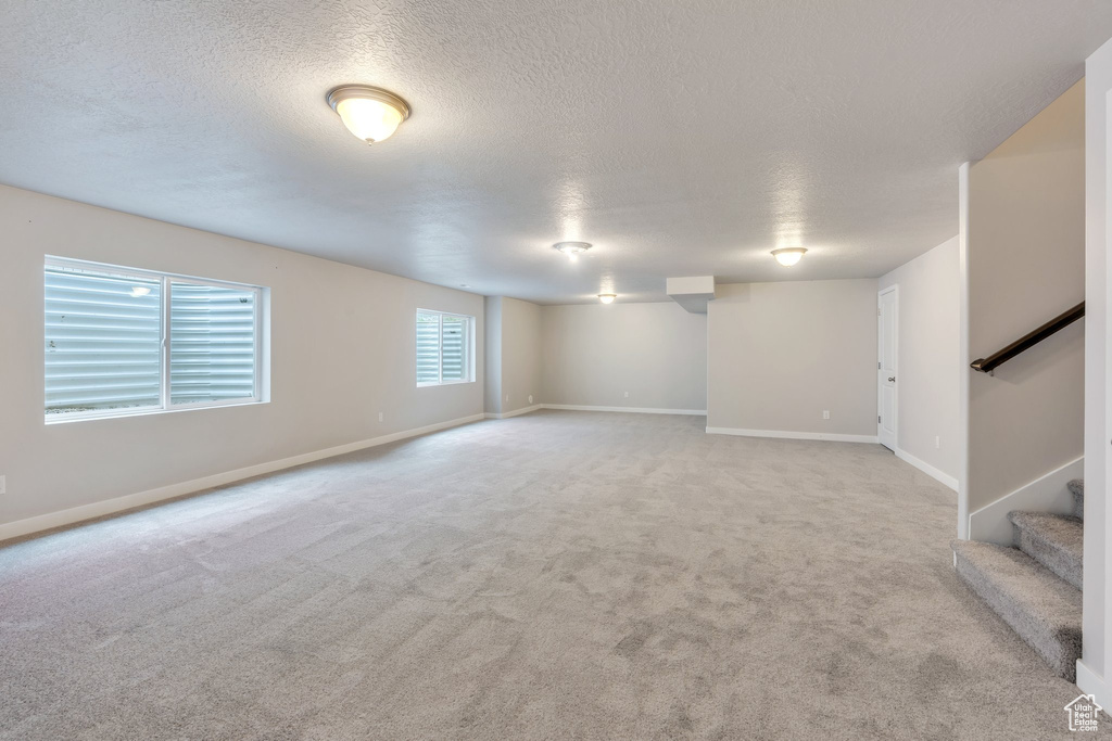 Below grade area with stairway, a textured ceiling, carpet flooring, and baseboards
