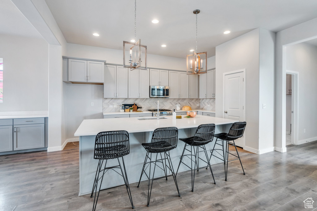 Kitchen featuring a kitchen island with sink, a sink, stainless steel microwave, tasteful backsplash, and light countertops
