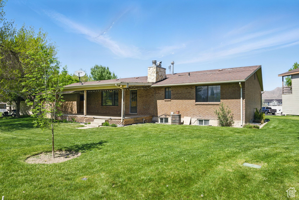 Back of property with a lawn, brick siding, a chimney, and a patio