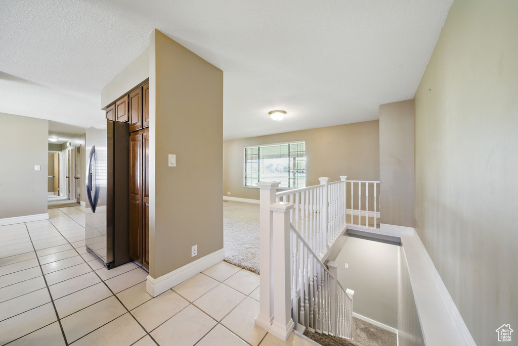 Hall featuring light tile patterned floors, baseboards, and an upstairs landing