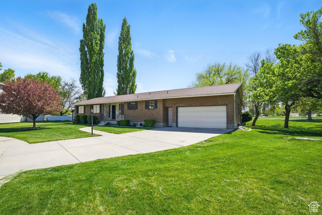 Ranch-style house featuring brick siding, a garage, a front lawn, and concrete driveway