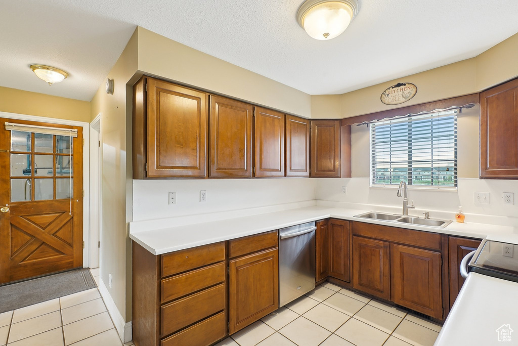 Kitchen featuring a sink, light tile patterned floors, stainless steel dishwasher, and light countertops