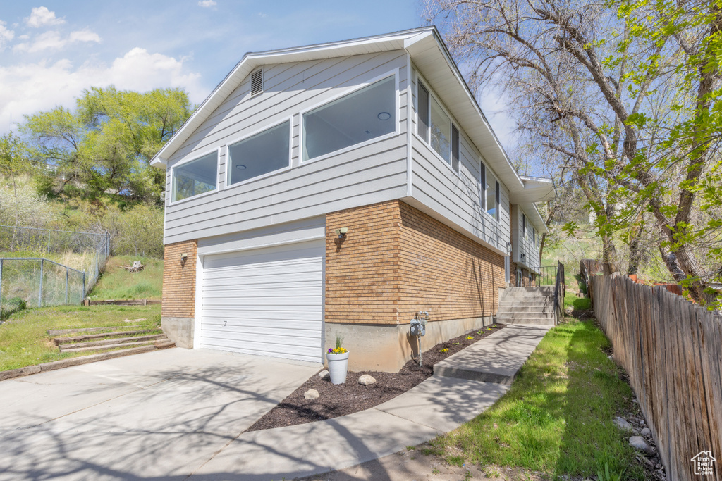 View of property exterior with brick siding, driveway, a garage, and fence