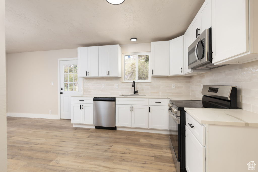 Kitchen featuring white cabinets, stainless steel appliances, a sink, baseboards, and backsplash
