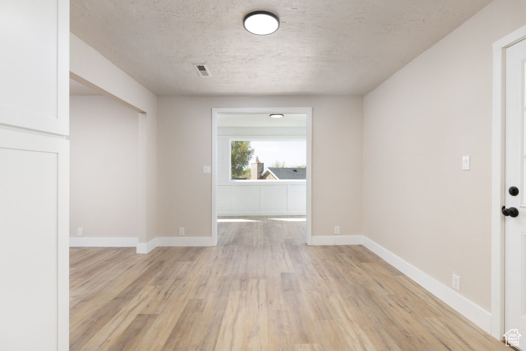 Spare room with baseboards, light wood finished floors, a textured ceiling, and visible vents