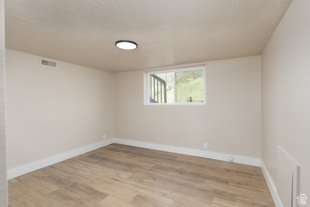 Spare room featuring baseboards, light wood-style floors, visible vents, and a textured ceiling