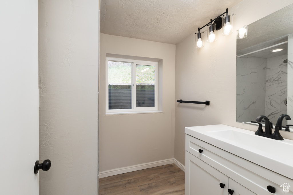Bathroom with wood finished floors, vanity, baseboards, a textured ceiling, and a shower