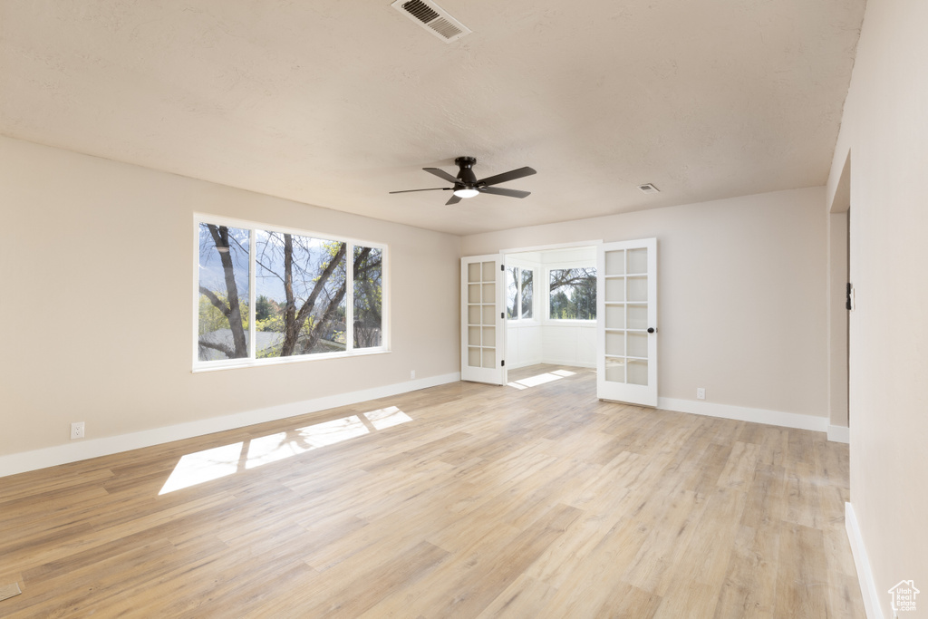 Spare room with a ceiling fan, french doors, light wood finished floors, baseboards, and visible vents