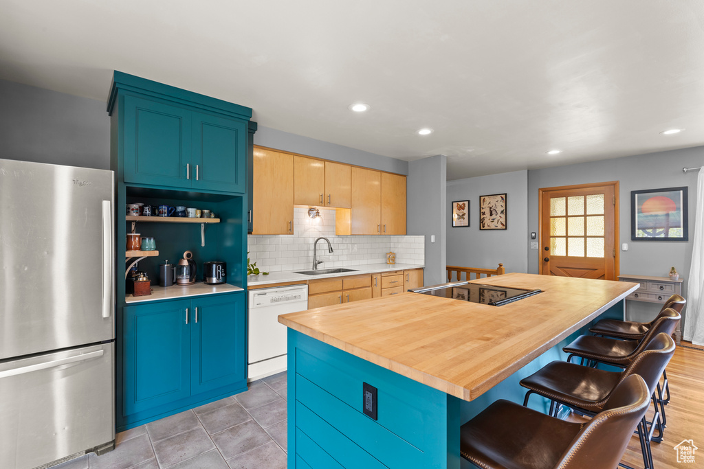 Kitchen with a breakfast bar, a sink, dishwasher, black electric cooktop, and freestanding refrigerator