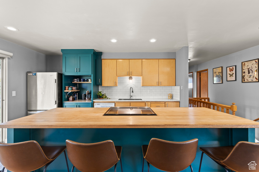 Kitchen featuring a breakfast bar, a sink, black electric cooktop, decorative backsplash, and butcher block counters