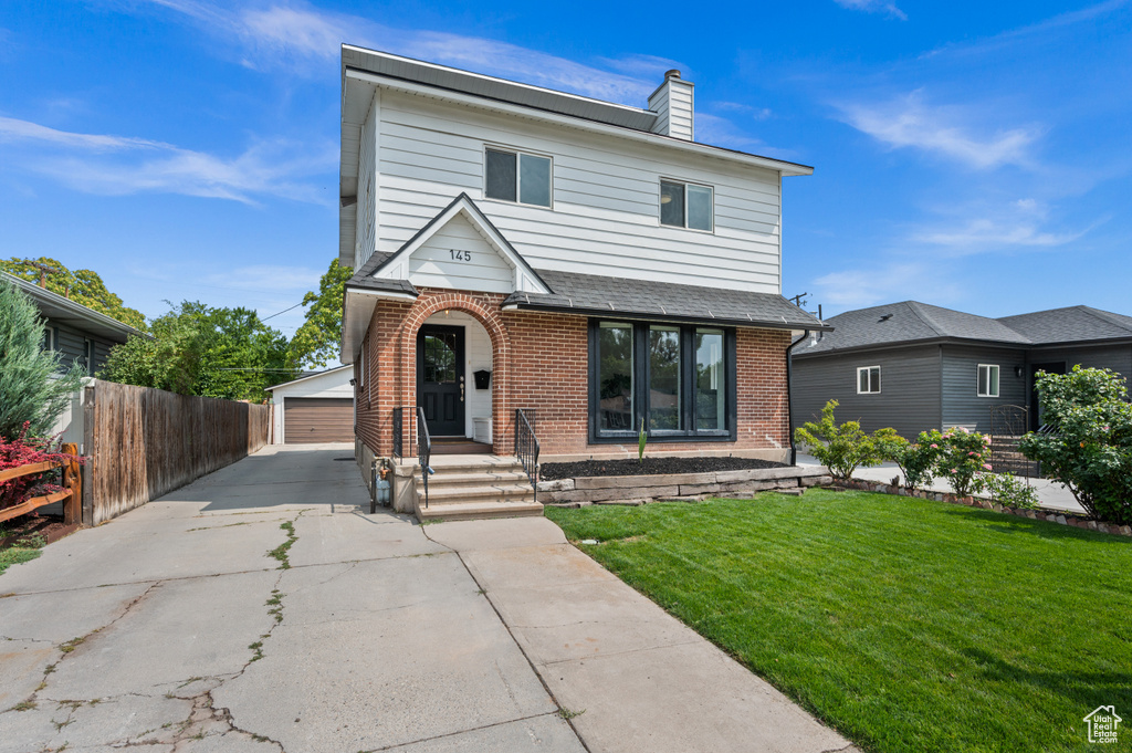 Traditional home featuring an outbuilding, fence, brick siding, a garage, and a front yard