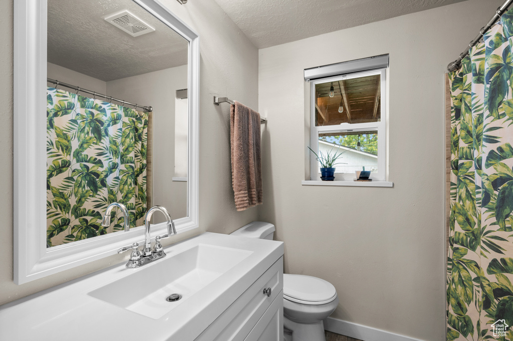 Bathroom featuring a textured ceiling, visible vents, toilet, and vanity