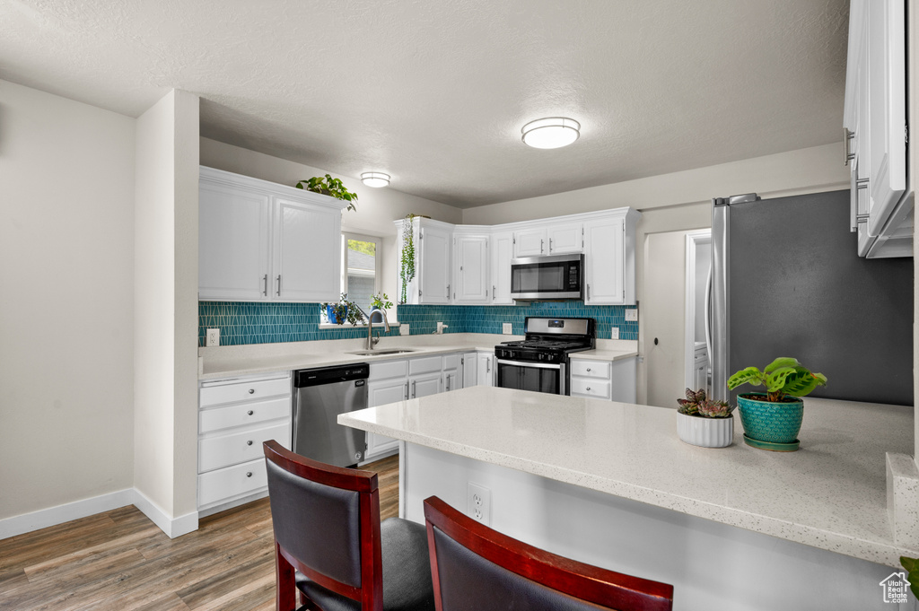 Kitchen featuring white cabinets, appliances with stainless steel finishes, a sink, and light wood finished floors