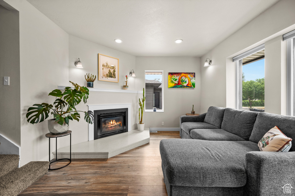 Living area with a glass covered fireplace, wood finished floors, a wealth of natural light, and recessed lighting