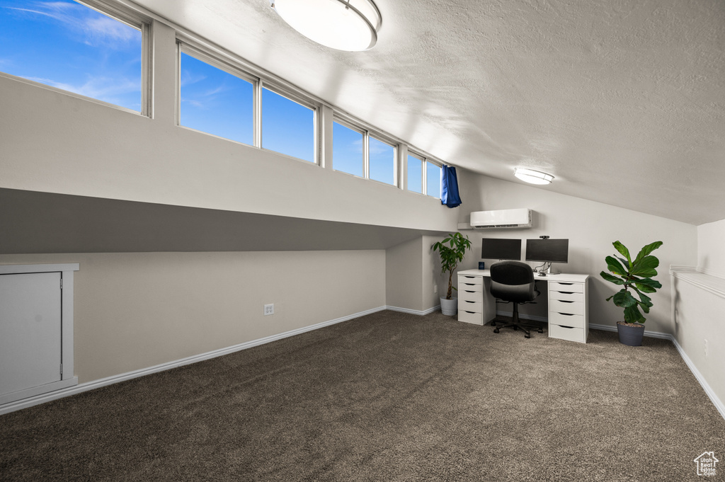 Carpeted home office with lofted ceiling, a textured ceiling, a wall mounted AC, and baseboards