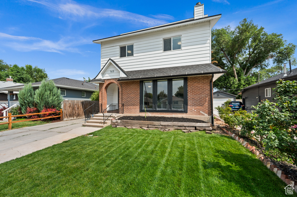 Traditional-style home with a chimney, fence, brick siding, a shingled roof, and a front yard